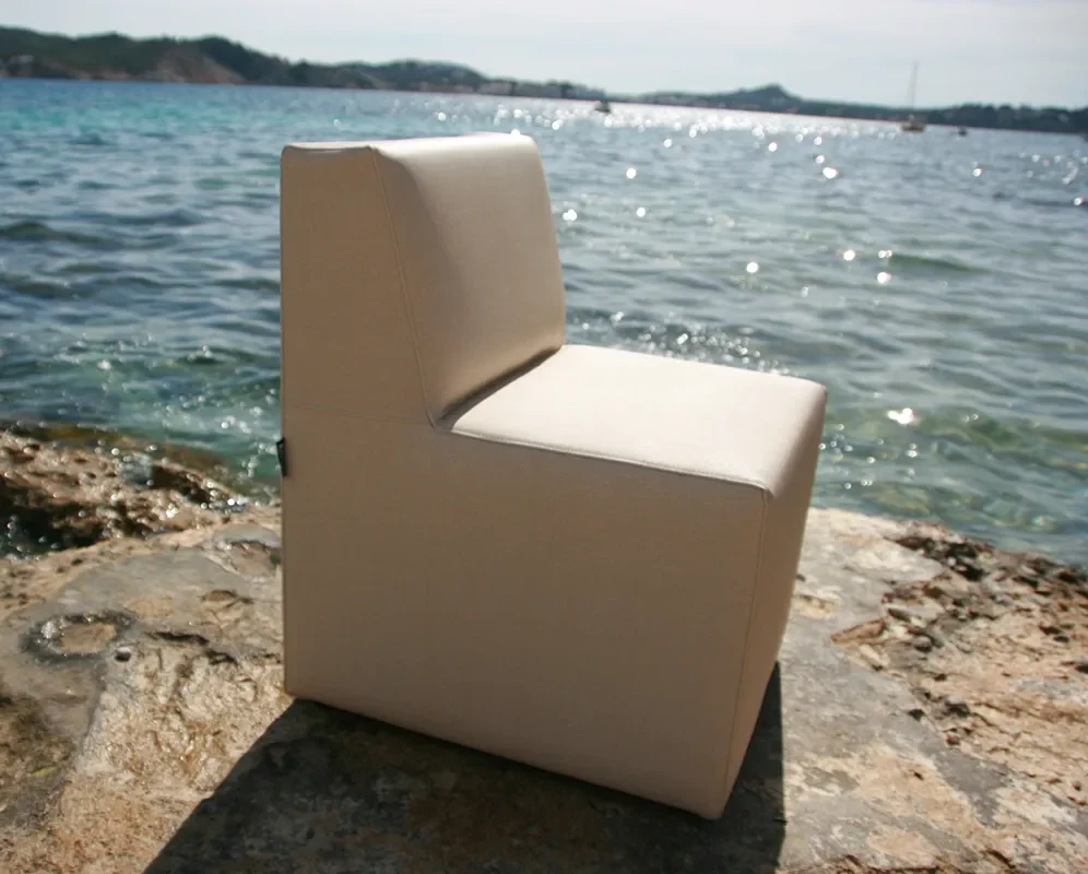 Sillón Balear tapizado en color claro sobre la arena junto al mar.